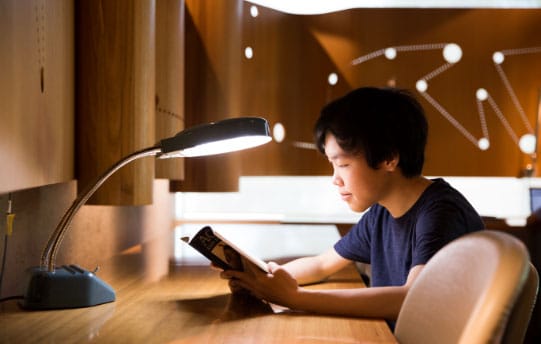 young man reading book in library with light