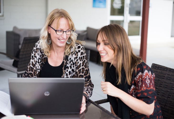 two women laughing while working on laptop
